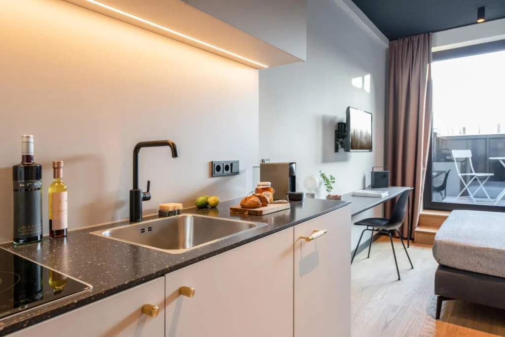 Kitchenette with sink and desk in front of floor-to-ceiling window in the XS apartment, ipartment Hamburg HafenCity