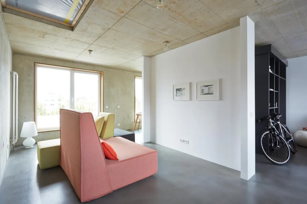 Living area with pink armchair, white divider and bicycle on the shelf in Apartment L, ipartment Cologne Mülheim
