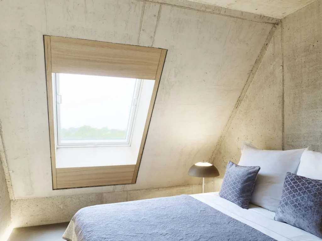 Double bed under the slanted roof window with concrete walls in Apartment M, ipartment Cologne Mülheim