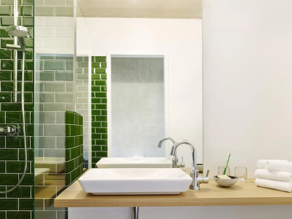 Bathroom with green tiles, built-in sink and shower area in Apartment M, ipartment Cologne Mülheim