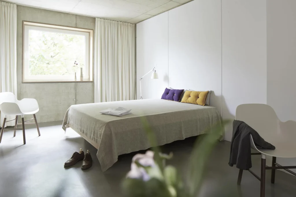 Sleeping area with a large bed, colorful pillows and windows to the greenery in Apartment S, apartment Cologne Mülheim