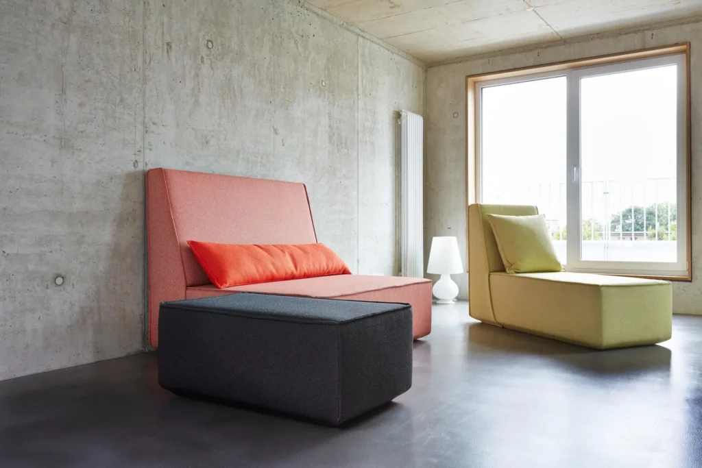 Lounge armchair in pink and yellow in front of a concrete wall and a floor-to-ceiling window in the XL apartment, ipartment Cologne Mülheim