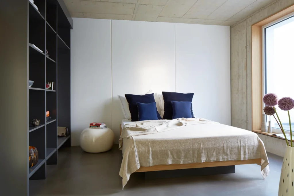 Sleeping area with double bed, dark blue pillows, dark shelf and large window in the XL apartment, ipartment Cologne Mülheim
