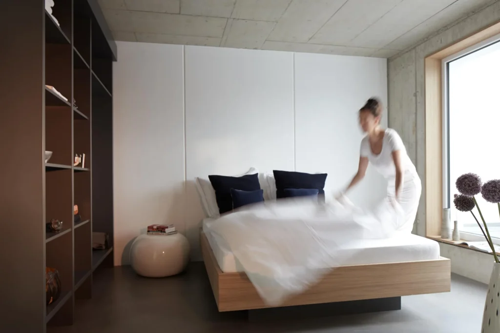 Woman takes the double bed out of the closet; in the background are a shelf and a window in the XL apartment, ipartment Cologne Mülheim