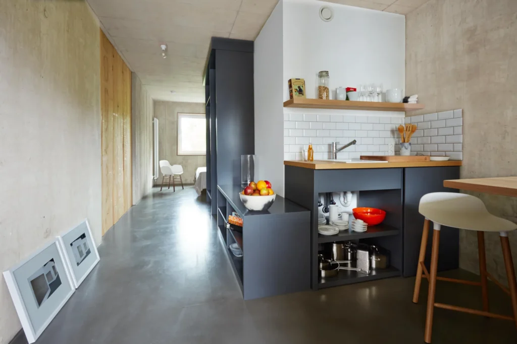 Longer living space with designer kitchen, bar stools and concrete walls in the XS apartment, ipartment Cologne Mülheim
