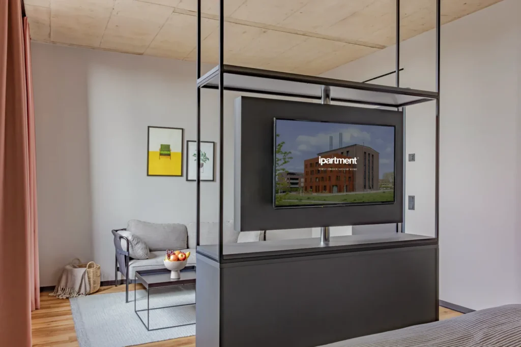 Sitting area with armchair and coffee table; in front of it is a shelving unit with a TV in the Luxury apartment, ipartment Leverkusen