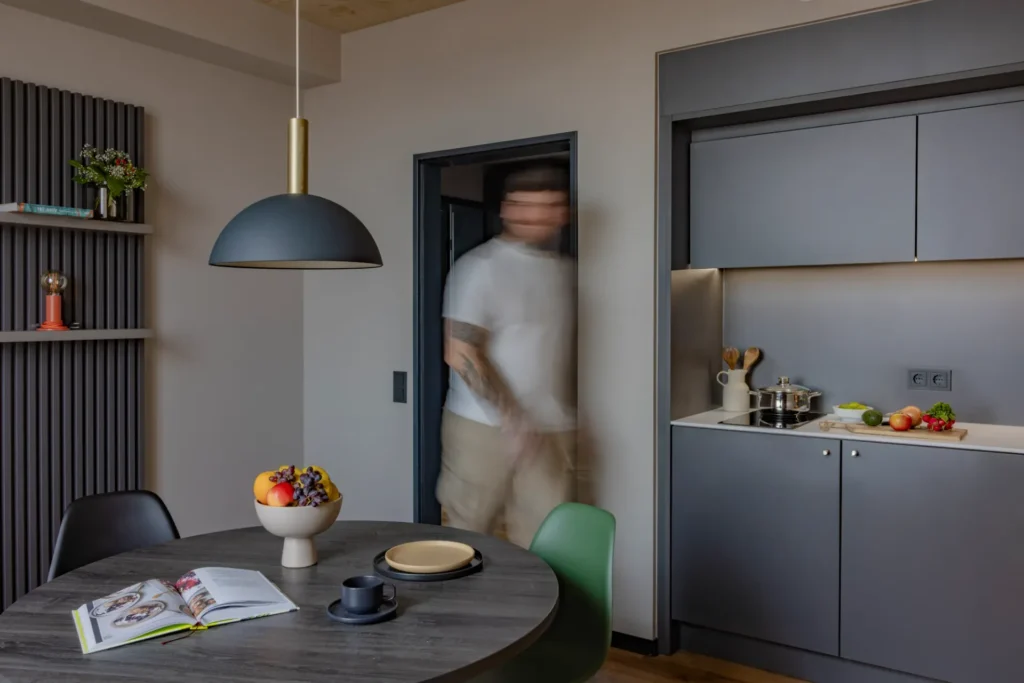 Dining table with fruit bowl and pendant light in front of the kitchenette with cooking stove in the Luxury apartment, ipartment Leverkusen
