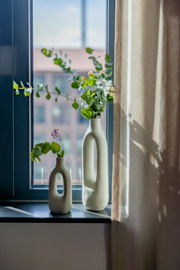 Window sill with two vases and flowers; next to it is a curtain and a view of brickwork in the Luxury apartment, ipartment Leverkusen