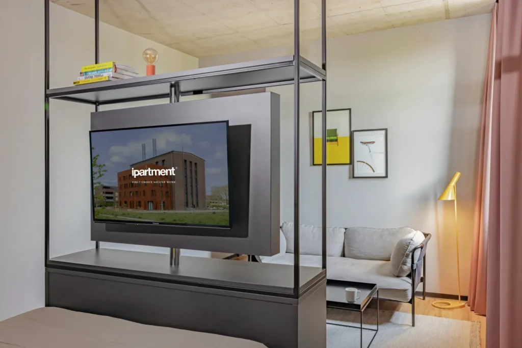 Living area with sofa, floor lamp and swivel TV on the shelf by the bed in the Medium apartment, ipartment Leverkusen