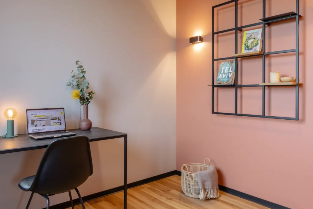 Desk with laptop and lamp, chair and metal shelf in front of a pink wall in the Xtra Luxury apartment, ipartment Leverkusen