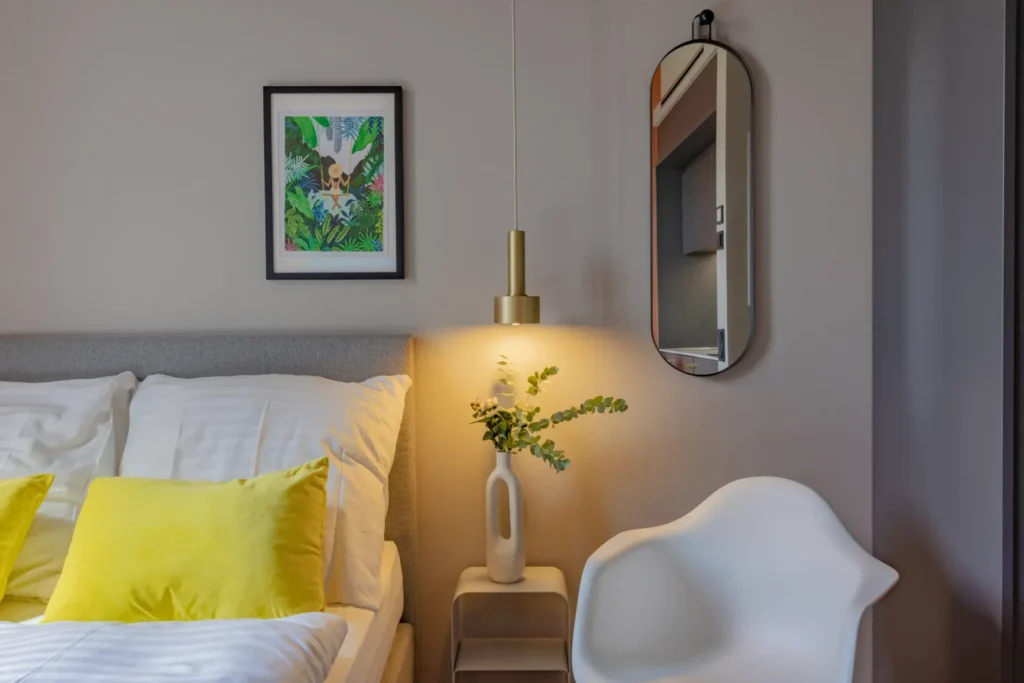 Double bed with yellow pillows, nightstand, wall mirror and picture in the Xtra Smart apartment, ipartment Leverkusen