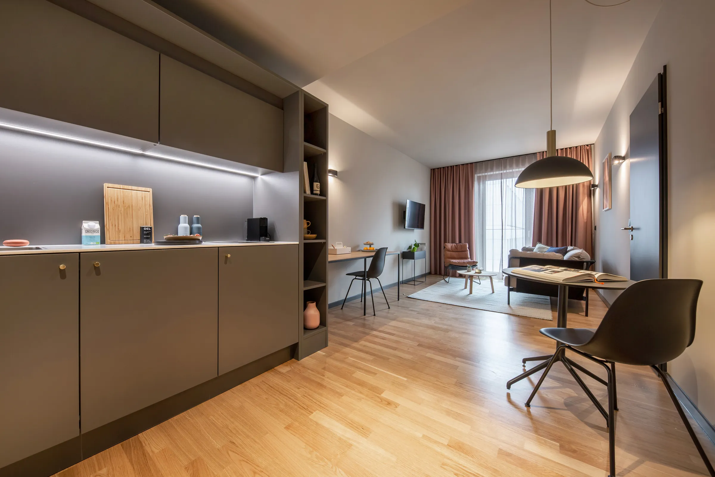 Möbliertes Serviced Apartment mit Küchenzeile, Arbeitsplatz und Wohnbereich mit Blick zu den Vorhängen