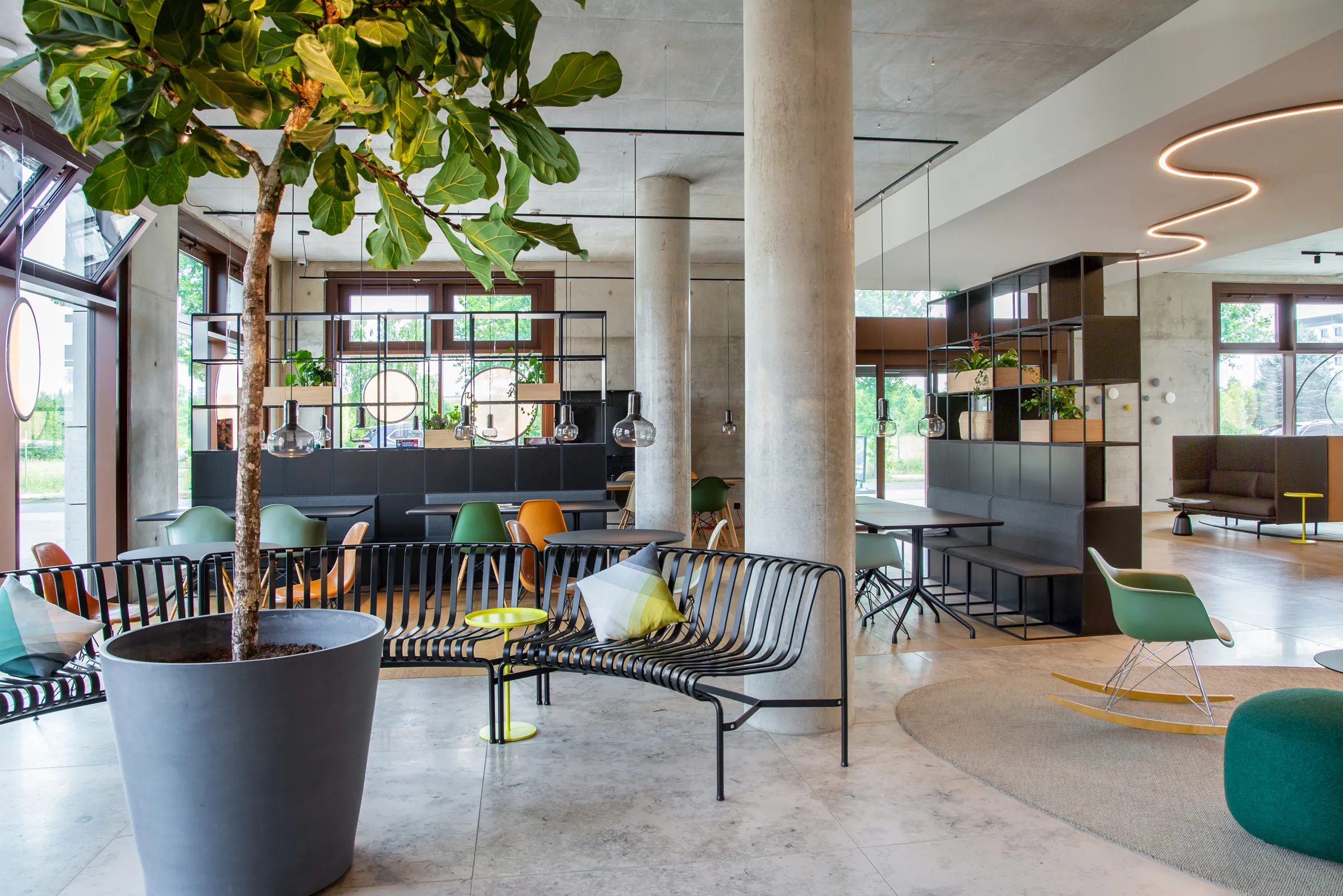 Helle Lounge mit Betonsäulen, Sitzbänken, grünen Schaukelstühlen, Zimmerpflanze und geschwungener Leuchtlinie an der Decke