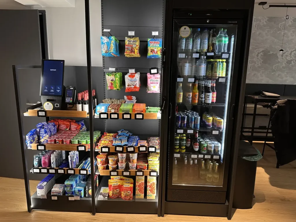 Regale mit Süßigkeiten und Snacks, ein Kühlschrank mit Getränken und ein Bezahlterminal.