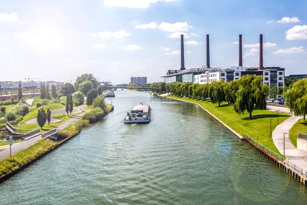 Sommerliches Panorama am Mittellandkanal in Wolfsburg mit Lastkahn und VW-Werk im Hintergrund