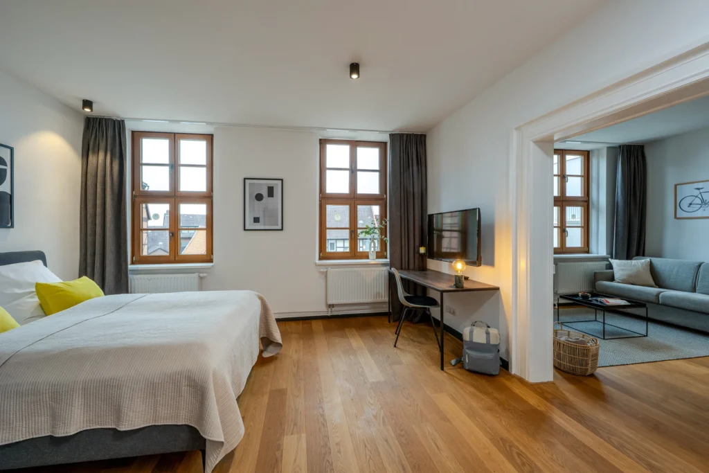 Sleeping area with double bed and desk, access to the living room with sofa, ipartment Wolfsburg