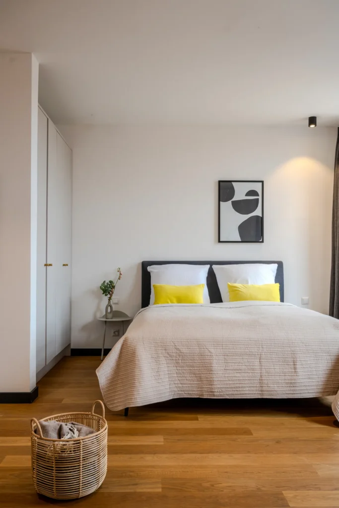 Double bed with yellow pillows and white wardrobe in a high-rise apartment building, ipartment Wolfsburg