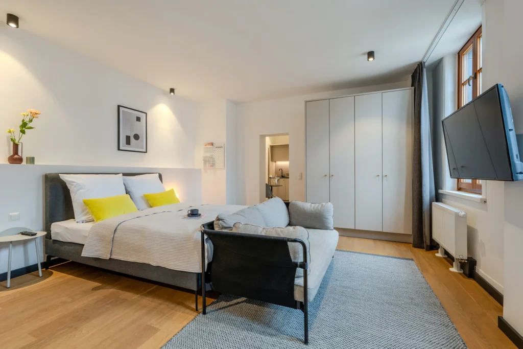 Double bed with sofa in front, wardrobe and access to the kitchen, ipartment Wolfsburg