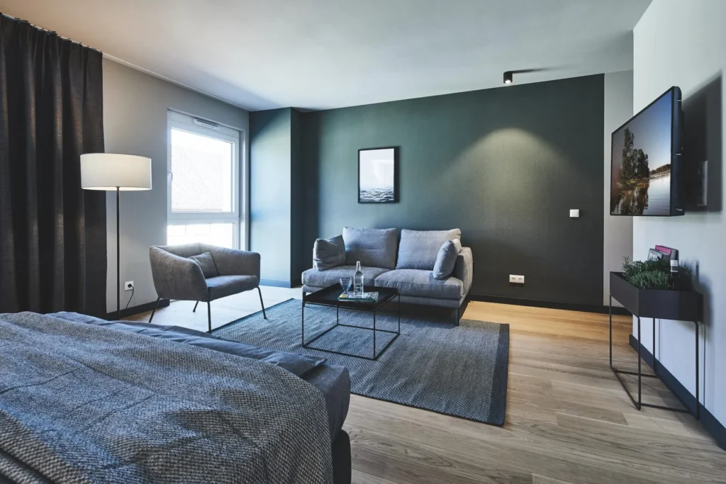 Living area with sofa, armchair and large-screen TV next to the bed in the XL apartment, ipartment Wolfsburg