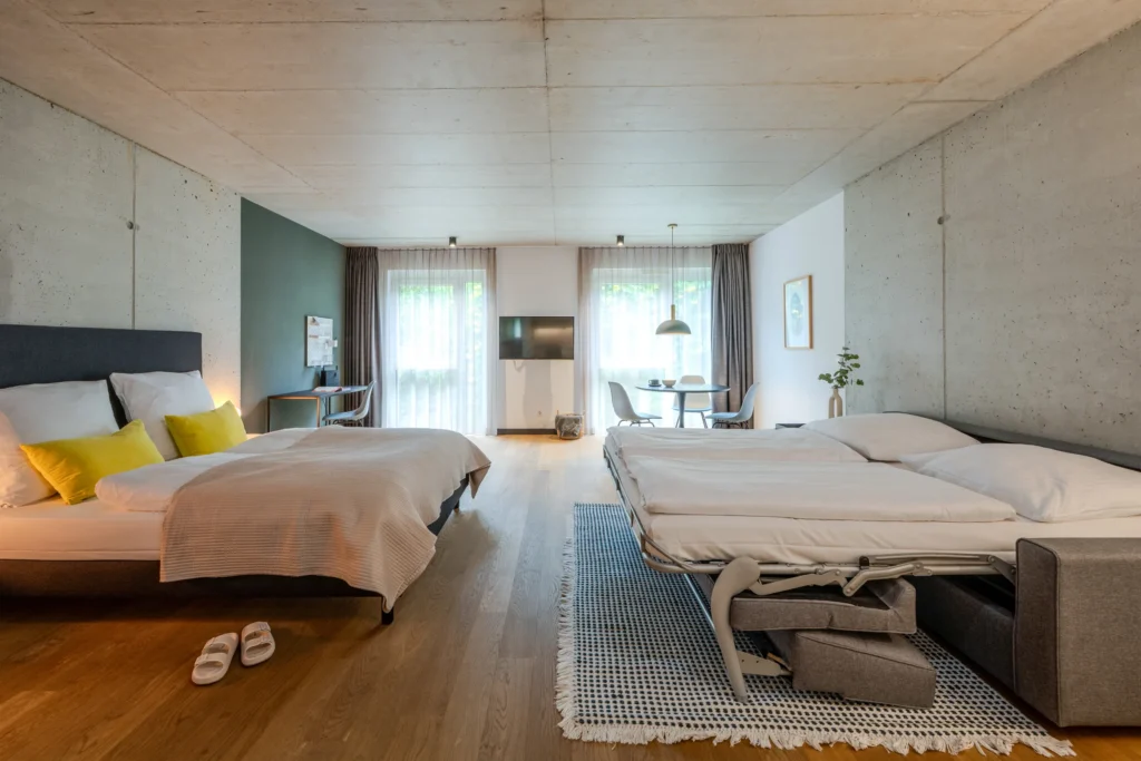 Double bed and folding sofa bed in the large room with exposed concrete, ipartment Wolfsburg