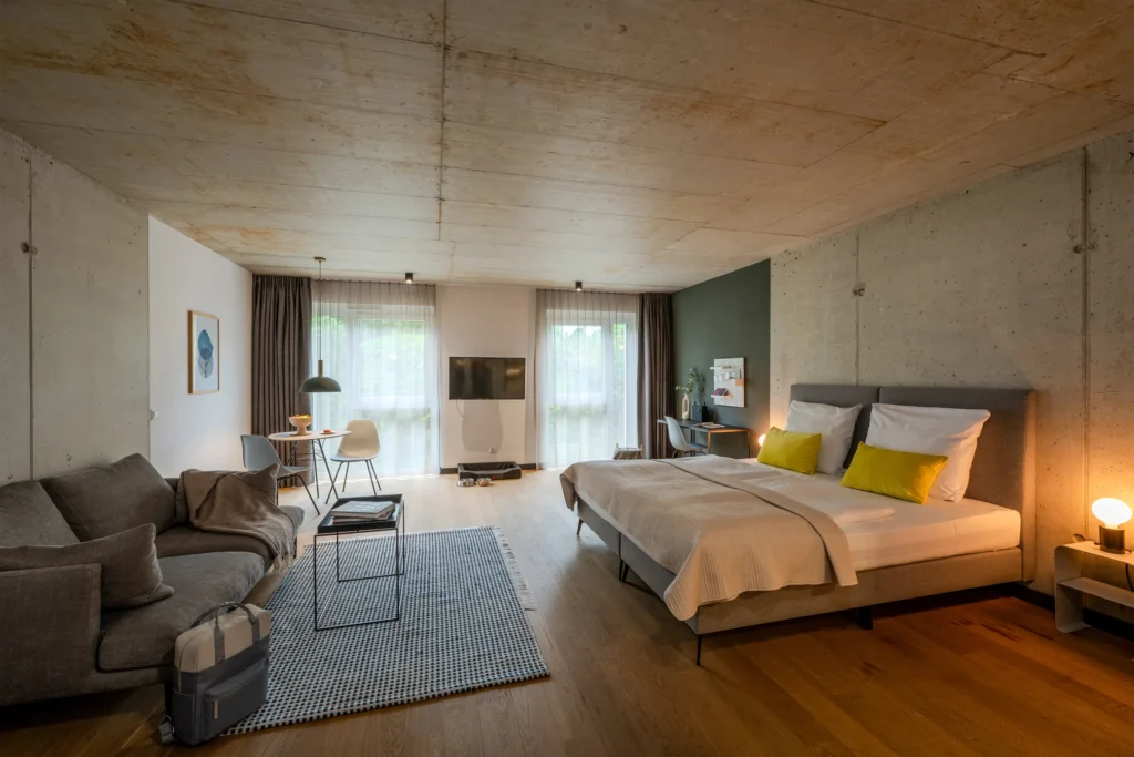Large room with a view ceiling, double bed, sofa and dining table, ipartment Wolfsburg
