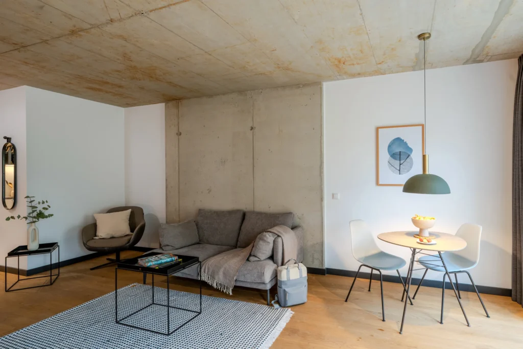 Living area with sofa, armchair, dining table and see-through concrete wall, ipartment Wolfsburg