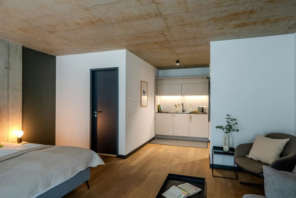 View from the bed towards the kitchen area and the sofa under the glazed concrete ceiling, ipartment Wolfsburg
