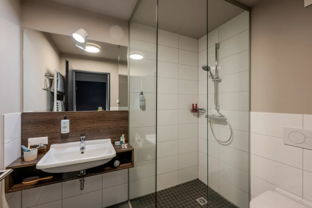 Bathroom with sink, mirror and shower behind glass, ipartment Wolfsburg