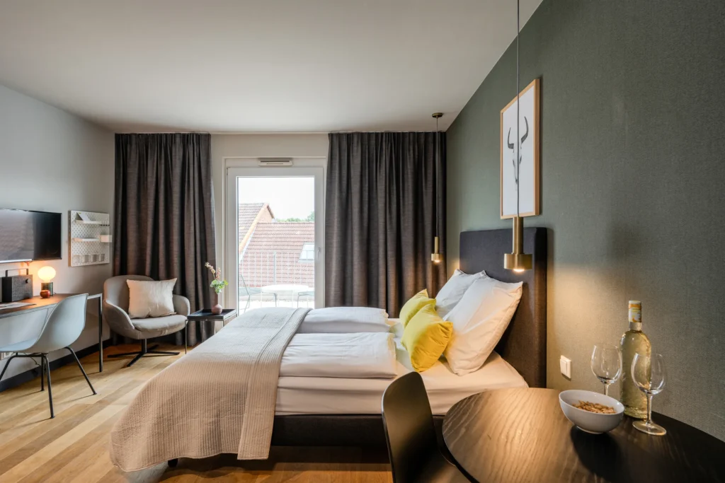 Double bed, armchair by the window, desk and round dining table, ipartment Wolfsburg