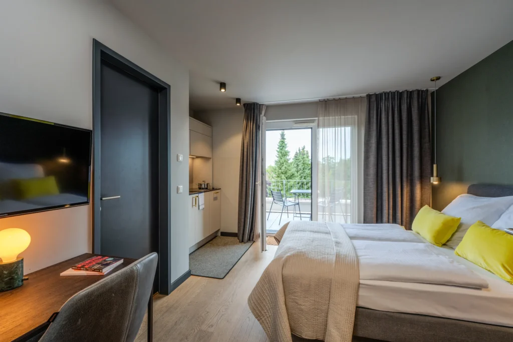 Double bed, kitchenette and desk with TV, window to the balcony, ipartment Wolfsburg