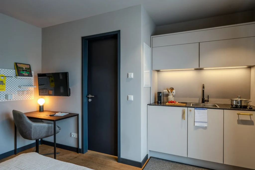 Desk with TV opposite the kitchen area, ipartment Wolfsburg