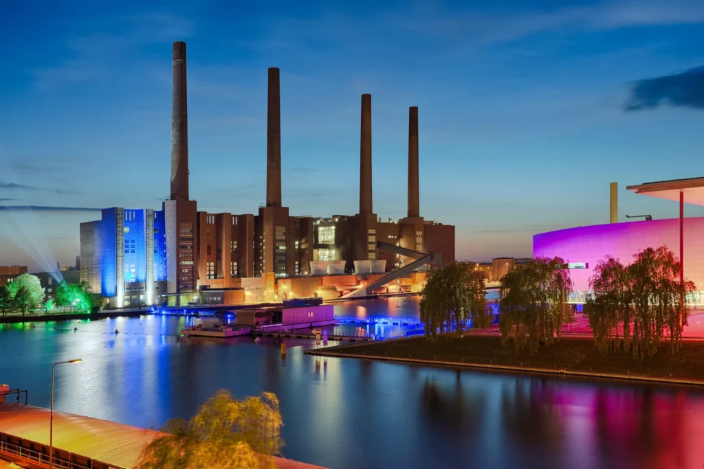 Illuminated power plant with four chimneys on the water at dusk in Wolfsburg