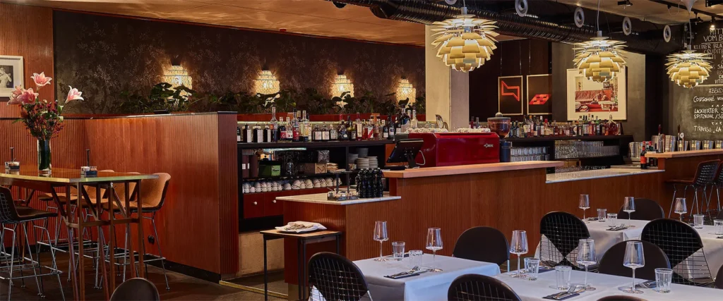 Restaurantinnenraum mit Holzbar, goldenen Pendelleuchten und gedeckten Tischen